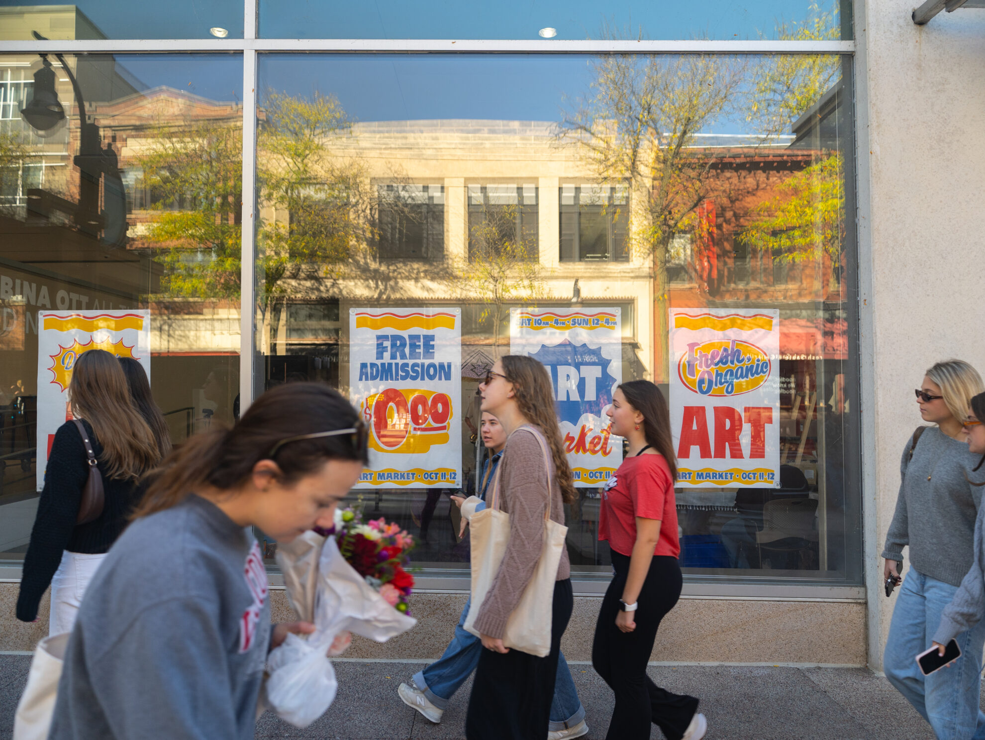 Students walking past a window with Art Market Posters